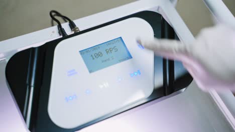woman's hand in white glove is switching on the tattoer machine. modern instrument for doing permanent make-up in a beauty salon. close-up