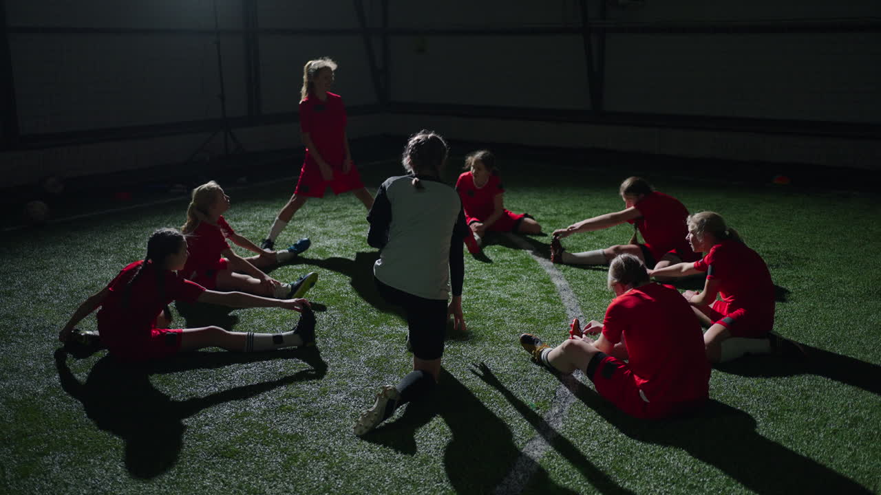 여자 축구 팀 이 실내 연습 중 스트레칭 을 하고 있다