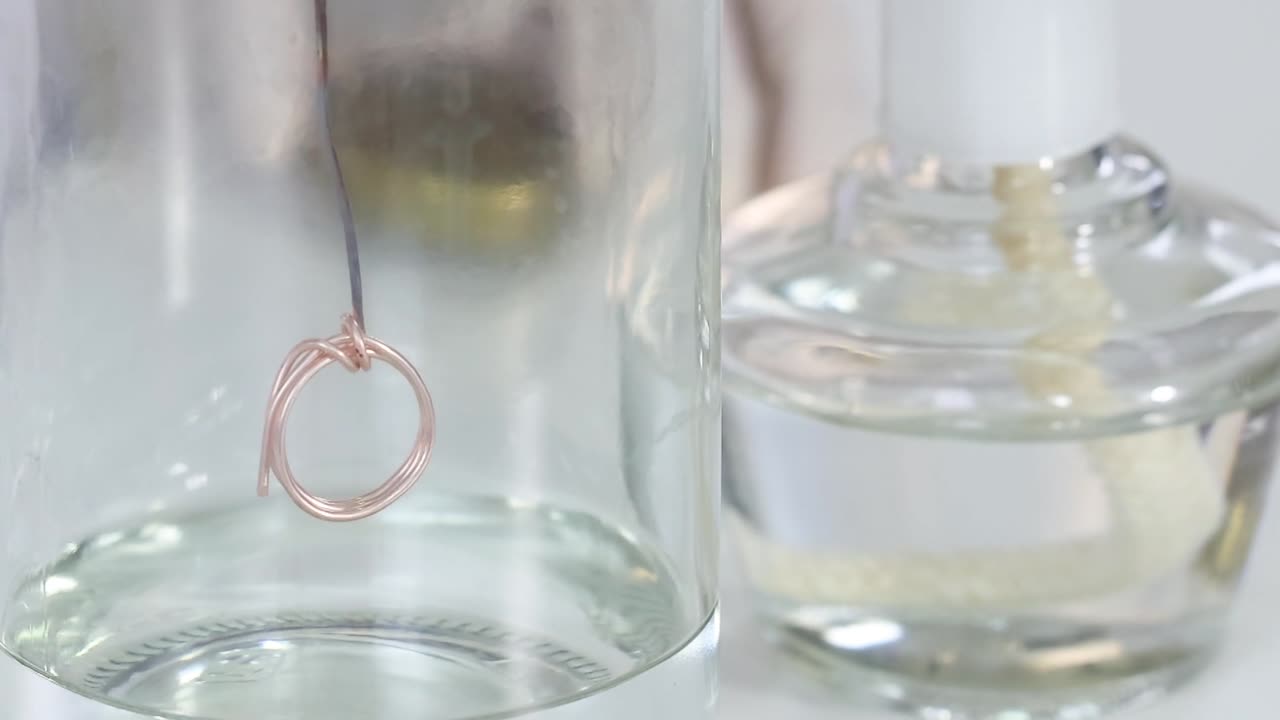 Close-up of a copper wire suspended in a glass flask containing a clear liquid.