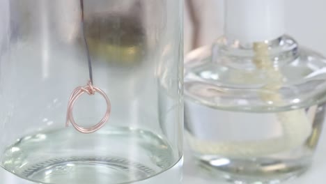 close-up of a copper wire suspended in a glass flask containing a clear liquid.