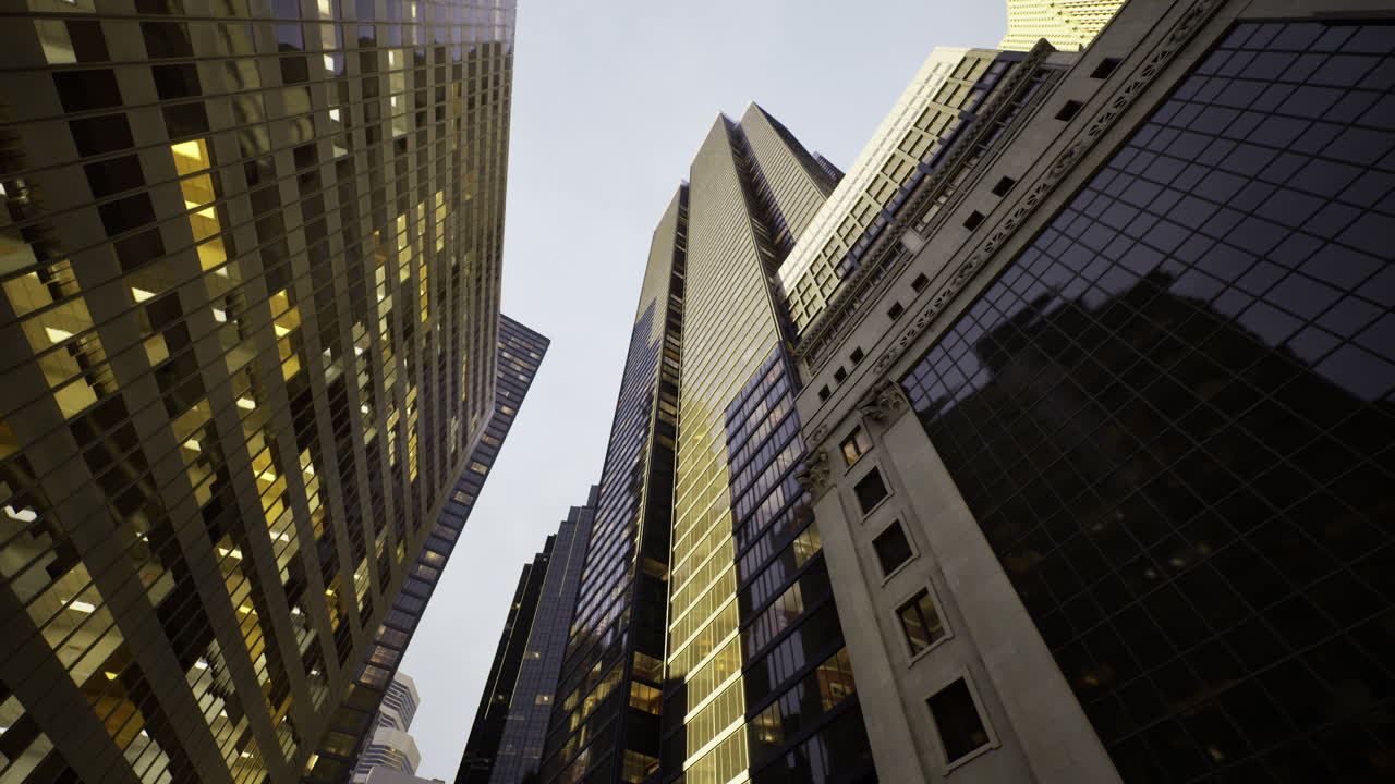 View from below of tall skyscrapers at dusk reflecting city lights