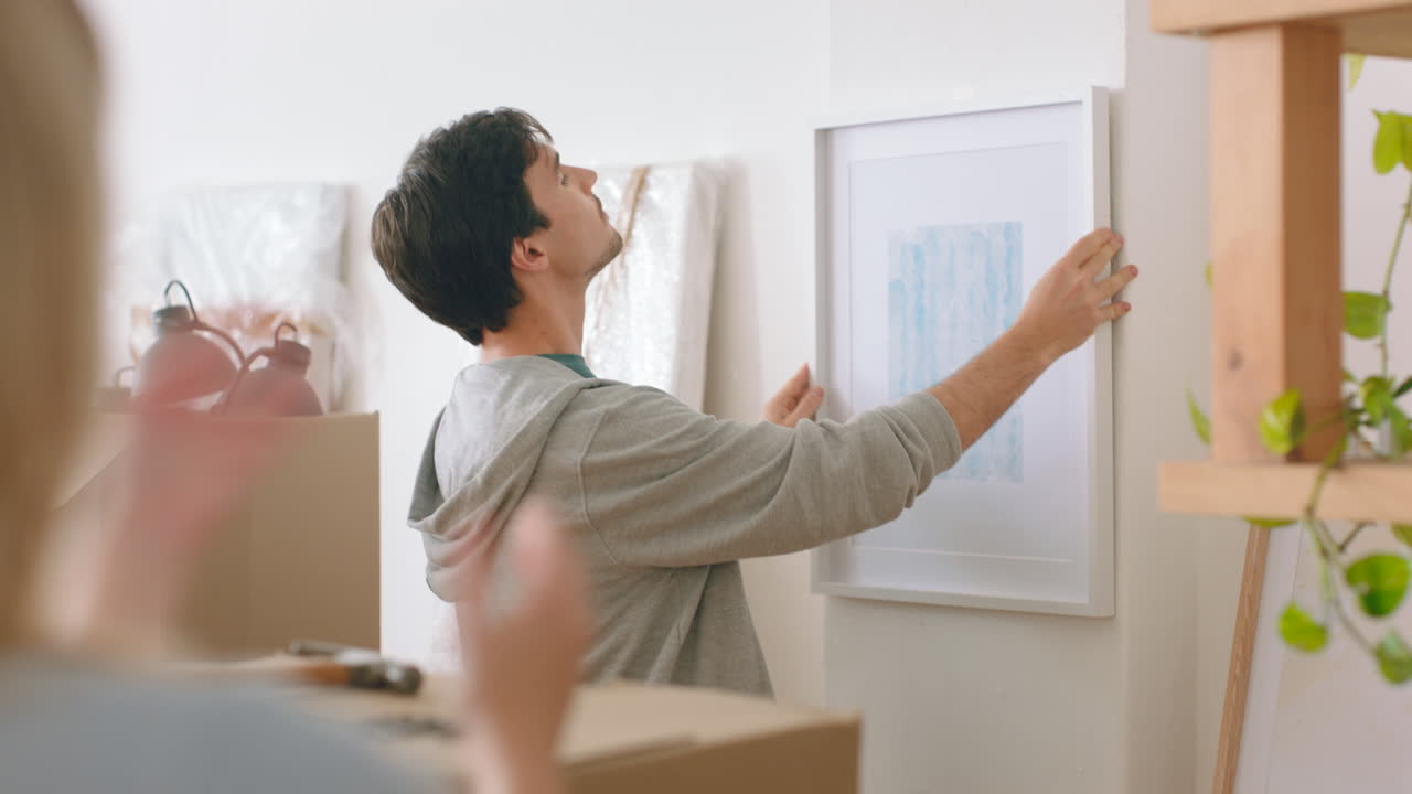 una pareja colgando un cuadro en un nuevo hogar.