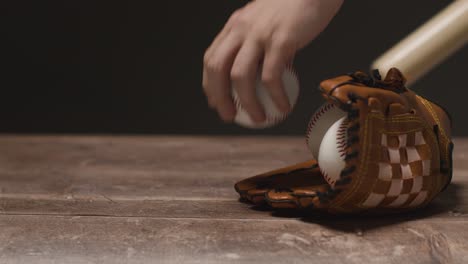 Studio-Baseballaufnahme-Mit-Fängerhandschuh-Und-Person,-Die-Holzschläger-Und-Ball-Vom-Holzhintergrund-Aufhebt