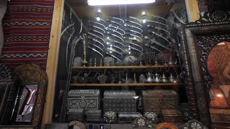 view from left to right of the wall of an antique shop decorated showcasing with variety of silver knives, wooden frame mirrors and filligree pattern trunk boxes.