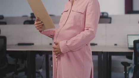 retrato de una mujer embarazada sonriente acariciando su vientre y sonriendo a la cámara en la oficina 1