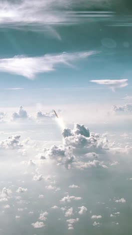 vertical shot of a space rocket or nuclear missile launching through the fluffy white clouds into a blue sky seen from above with long exhaust trail