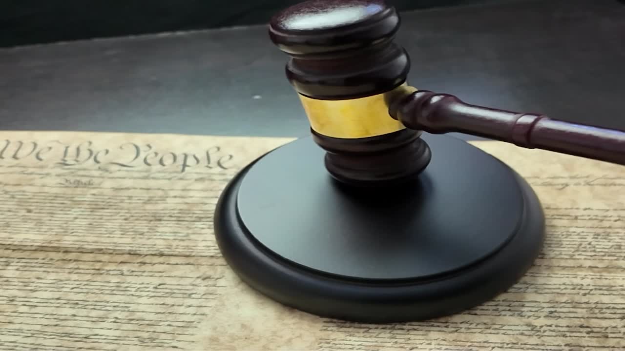 Un martelletto da giudice in legno appoggiato su una copia della Costituzione degli Stati Uniti, a simboleggiare le fondamenta del diritto, della giustizia e dell'autorità costituzionale americana. L'immagine rappresenta lo stato di diritto.