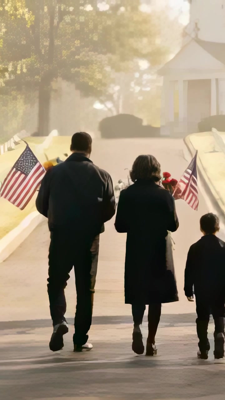 Vertical video: Walking family leaving memorial in coats carrying bouquet toward chapel with flags