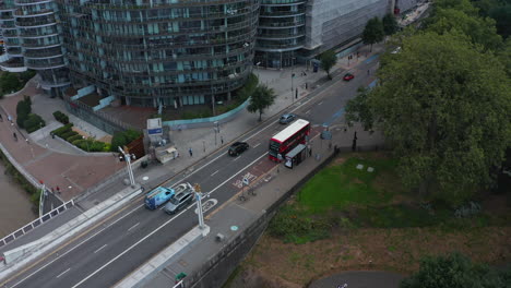 Aerial-view-of-road-in-modern-residential-district.-Rounded-apartment-complex.-Red-double-decker-standing-on-bus-stop.-London,-UK