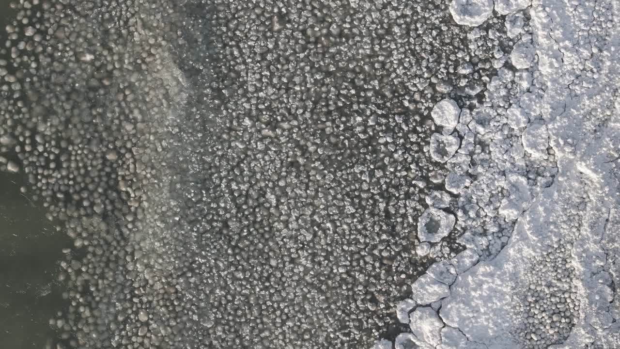A frozen lake with intricate ice patterns and clear water at the edge, aerial view