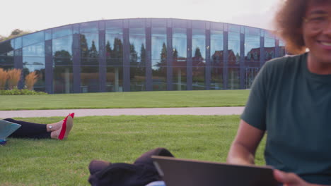 group of university or college students sit on grass outdoors on campus talking and working