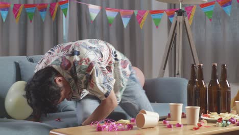 hombre sentado en el sofá después de una fiesta, mirando angustiado
