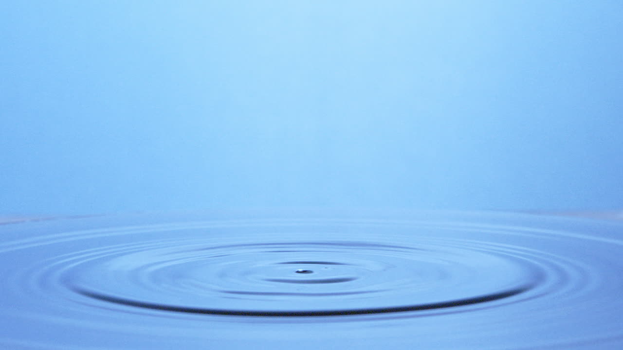 슬로우 모션 샷, 밝은 파란색 표면에 떨어지는 두 방울의 물이 물기둥을 만듭니다.