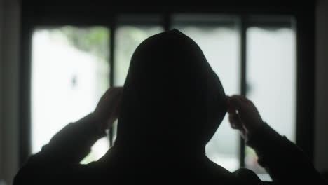 person in a hoodie looking out a window