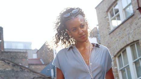 joven negra de moda en vestido azul de pie a la luz del sol en la calle, retroiluminada, ángulo bajo