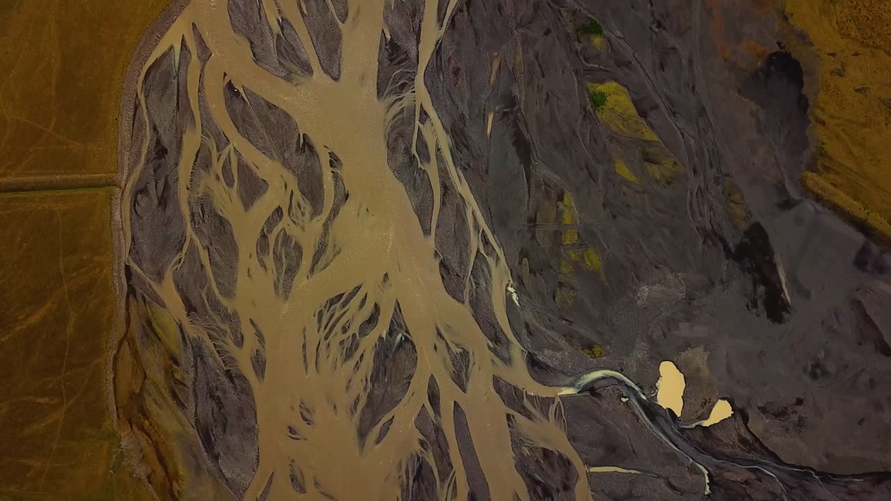 vista aérea superior de un río glaciar que fluye en un valle, con muchas ramas, sobre arena oscura, islandia