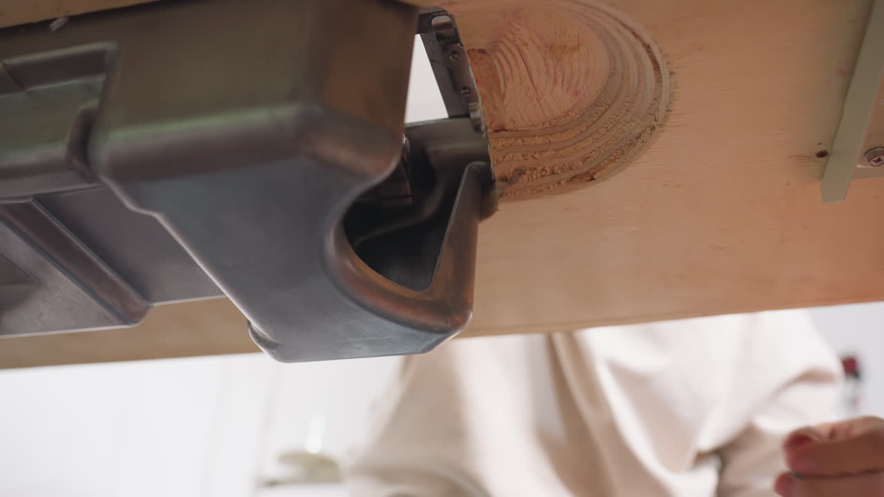 Under table view of sewing machine as designer reaches underneath to adjust mechanical parts, with hand and arm visible working on metal casing attached to wooden surface in workshop environment