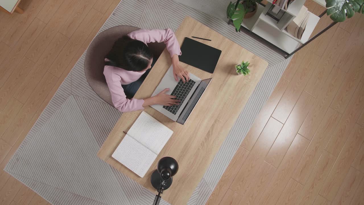 Top View Zoom Out Shot Of A Woman Typing On A Laptop While Sitting At The Wooden Desk At Home