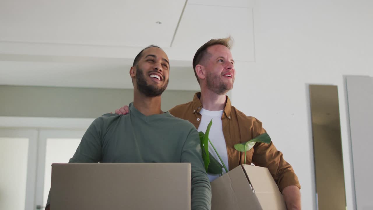 pareja de hombres homosexuales multiétnicos llevando cajas de embalaje a la casa