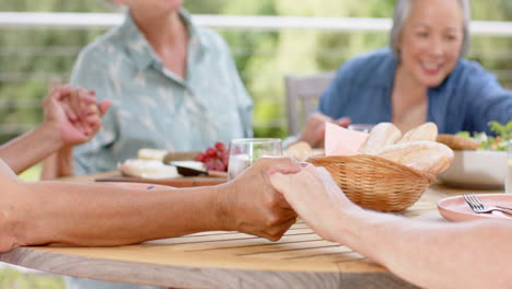 senior biracial woman holding hands with a caucasian woman at a meal, with copy space