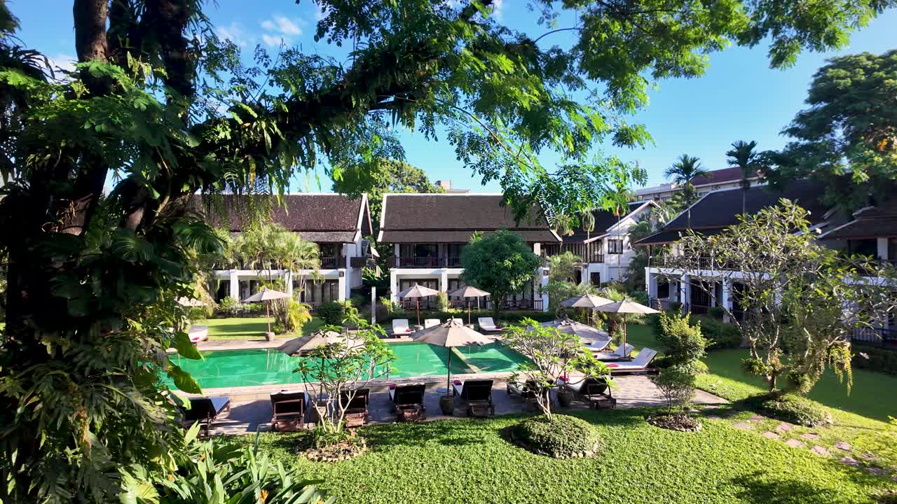 Boutique resort with a green swimming pool and sun loungers surrounded by lush gardens