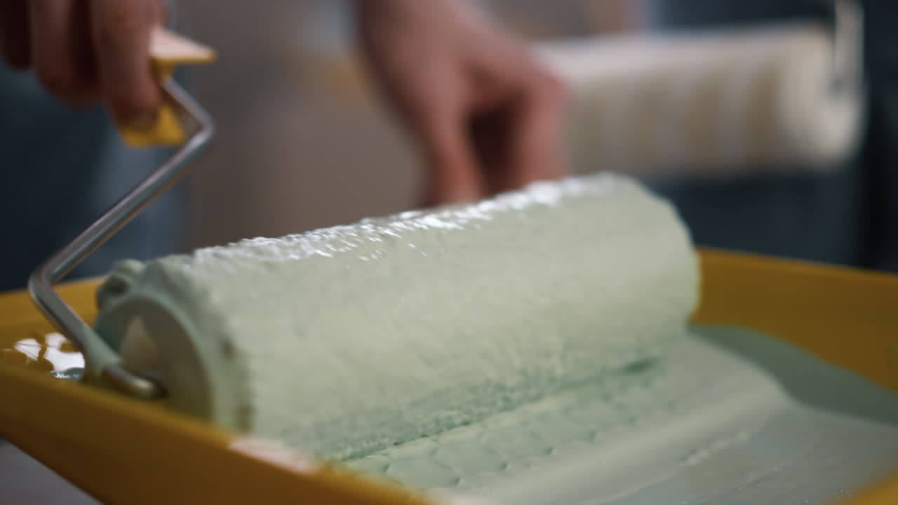 노란색 트레이에 있는 롤러에서 과도한 페인트를 제거하는 남자. 클로즈업 페인트 롤러.