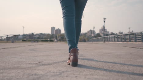 camera tracking woman's lower body as she walks along an empty street, focused on her stride, in brown boots and jeans