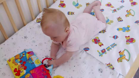 baby lays on her tummy while pulling her foam toy book towards her inside of her cot
