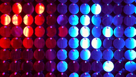 shiny kinetic surface panel illuminated by red and purple light in luxury boutique. flickering background for interruptions or text savers. mirror sequins sway by wind blowing.