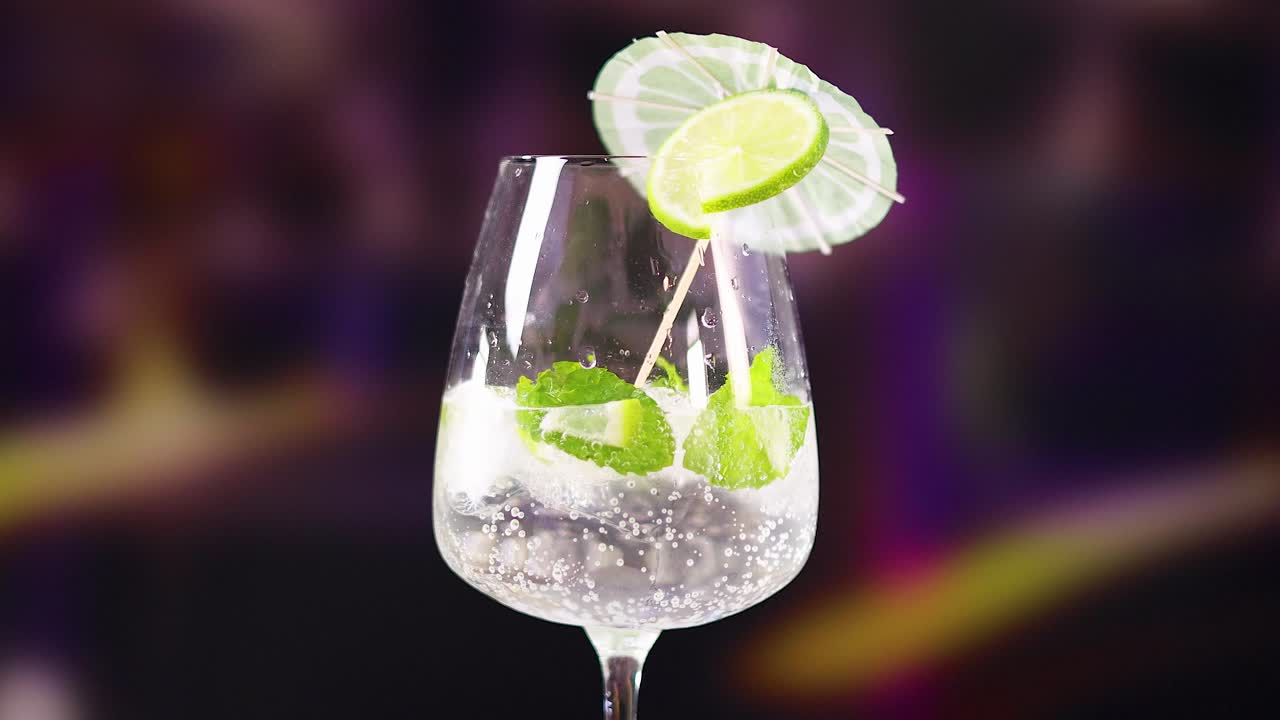 A mojito cocktail is artfully prepared with lime and mint in a lively, colorful environment. Bright lighting enhances the refreshing vibe