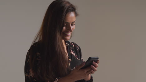 fotografía de estudio de una mujer sonriente con teléfono móvil recibiendo buenas noticias contra un fondo gris