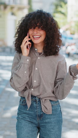 Mujer-Sonriente-Feliz-Teniendo-Una-Conversación-Remota-Hablando-Por-Teléfono-Inteligente-Chismes-De-Buenas-Noticias-En-Las-Calles-De-La-Ciudad