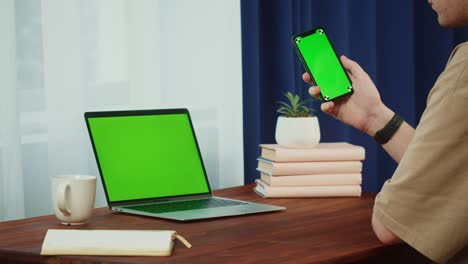 estudiante usando teléfono inteligente y portátil con llave de croma de primer plano. joven sosteniendo teléfono móvil con pantalla verde. hombre de negocios usa computadora, desplazando la pantalla verde del teléfono celular.