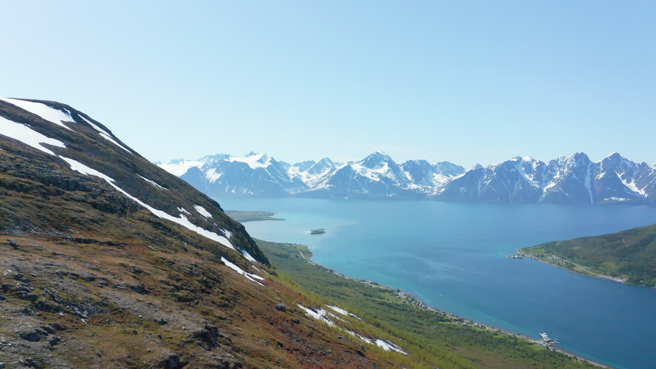 aéreo, en ascenso, drone disparó sobre una montaña nevada, hacia el océano ártico y el fiordo lyngen en el fondo, soleado, día de verano, en rotsund, nordland, noruega