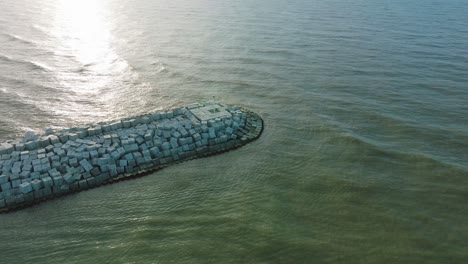 aerial birdseye view of protective pier with concrete blocks and rocks at baltic sea coastline at liepaja, latvia, strengthening beach against coastal erosion, drone shot moving forward tilt down