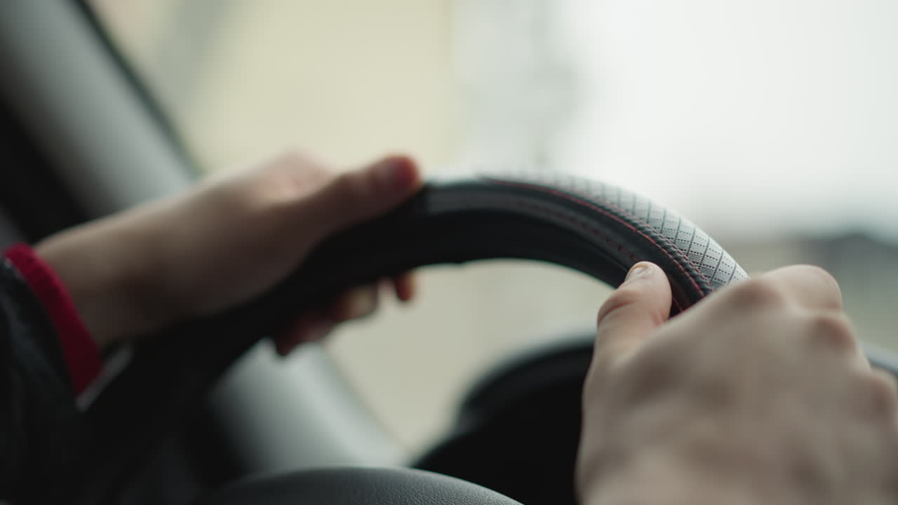 Pair of motorist hands on steering wheel controlling vehicle with gentle grip during urban drive, emphasizing smooth motion, focused posture and safe steering with natural light and cabin detail