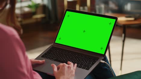 mujer adulta joven trabajando desde el apartamento del loft de la casa en una computadora portátil con pantalla verde. mujer creativa usando trackpad y navegando por internet. close up sobre el hombro.