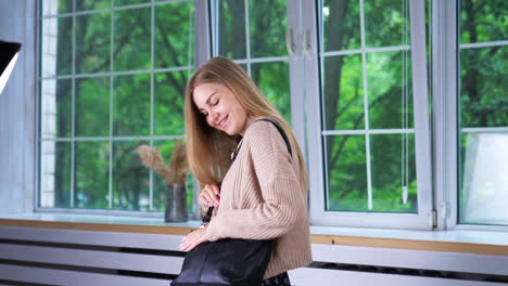 good-looking young fashionable lady in sweater in light skirt indoors. model posing in modern clothes with a black bag and black boots on tractor soles.