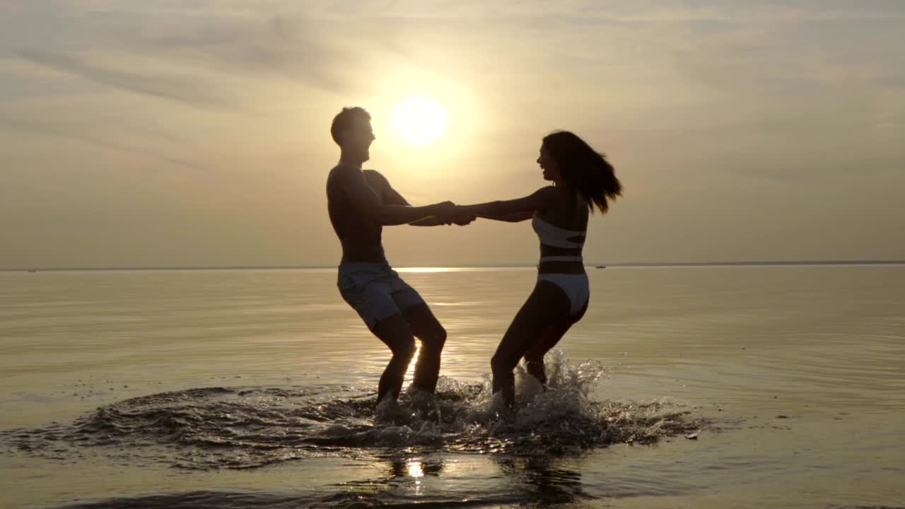 해가 지는 배경에서 물 위에서 회전하는 커플. 느린 동작