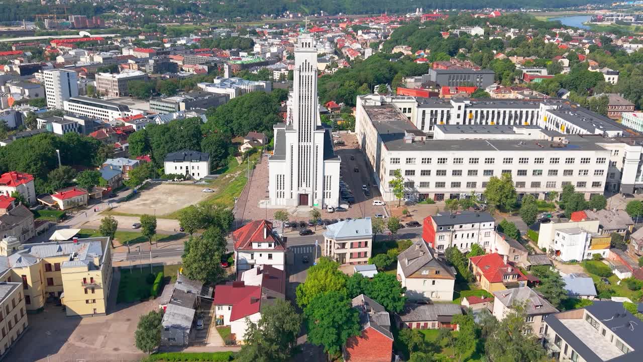 Drone view of Resurrection Church in Kaunas, Lithuania, showcasing modernist architecture surrounded by the city’s vibrant urban layout and lush green surroundings on a clear summer day, zooming in