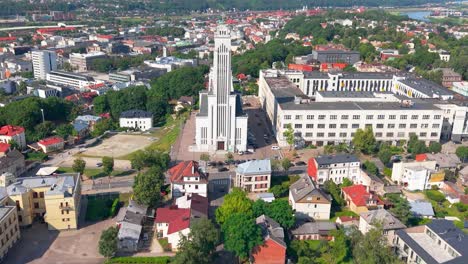 drone view of resurrection church in kaunas, lithuania, showcasing modernist architecture surrounded by the city’s vibrant urban layout and lush green surroundings on a clear summer day, zooming in