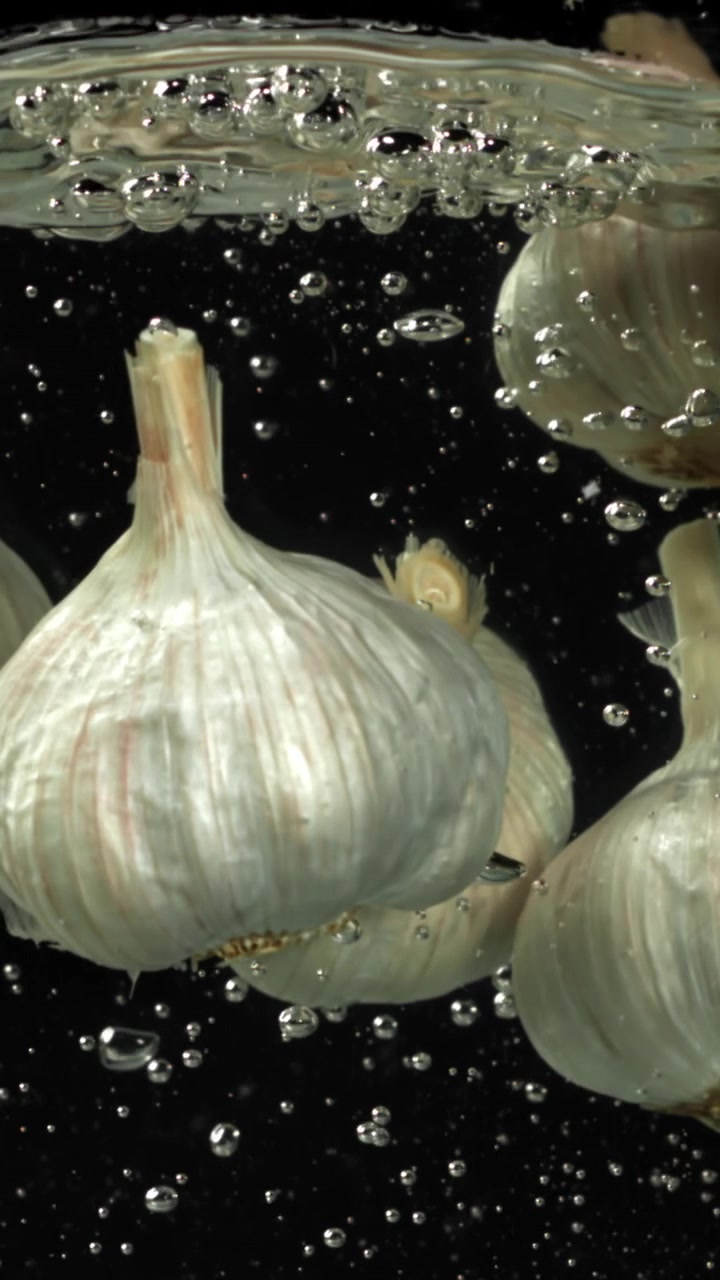 Bulbi d'aglio freschi immersi nell'acqua con bolle d'aria