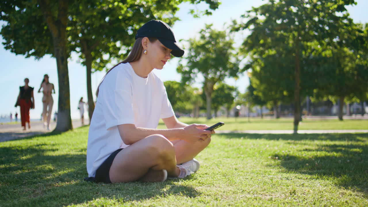 Girl watching social media on mobile phone sitting vivid sunny park grass