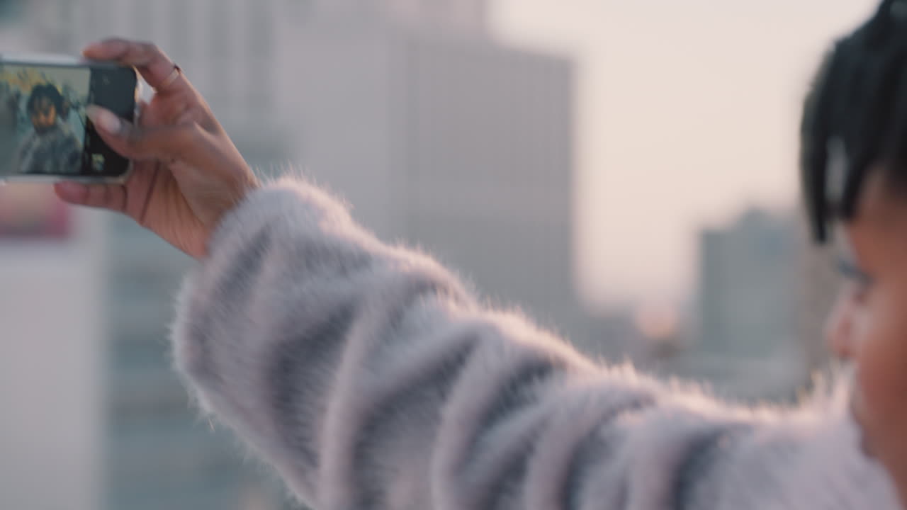 젊은 아프리카계 미국인 여성이 스마트폰 모바일 카메라를 사용하여 셀피 사진을 찍고 관광을 즐기며 휴가 사진을 소셜 미디어에 공유합니다.