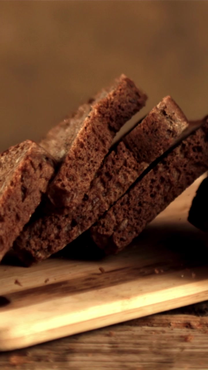 Fette di pane scuro ai semi che cadono al rallentatore su un tagliere di legno