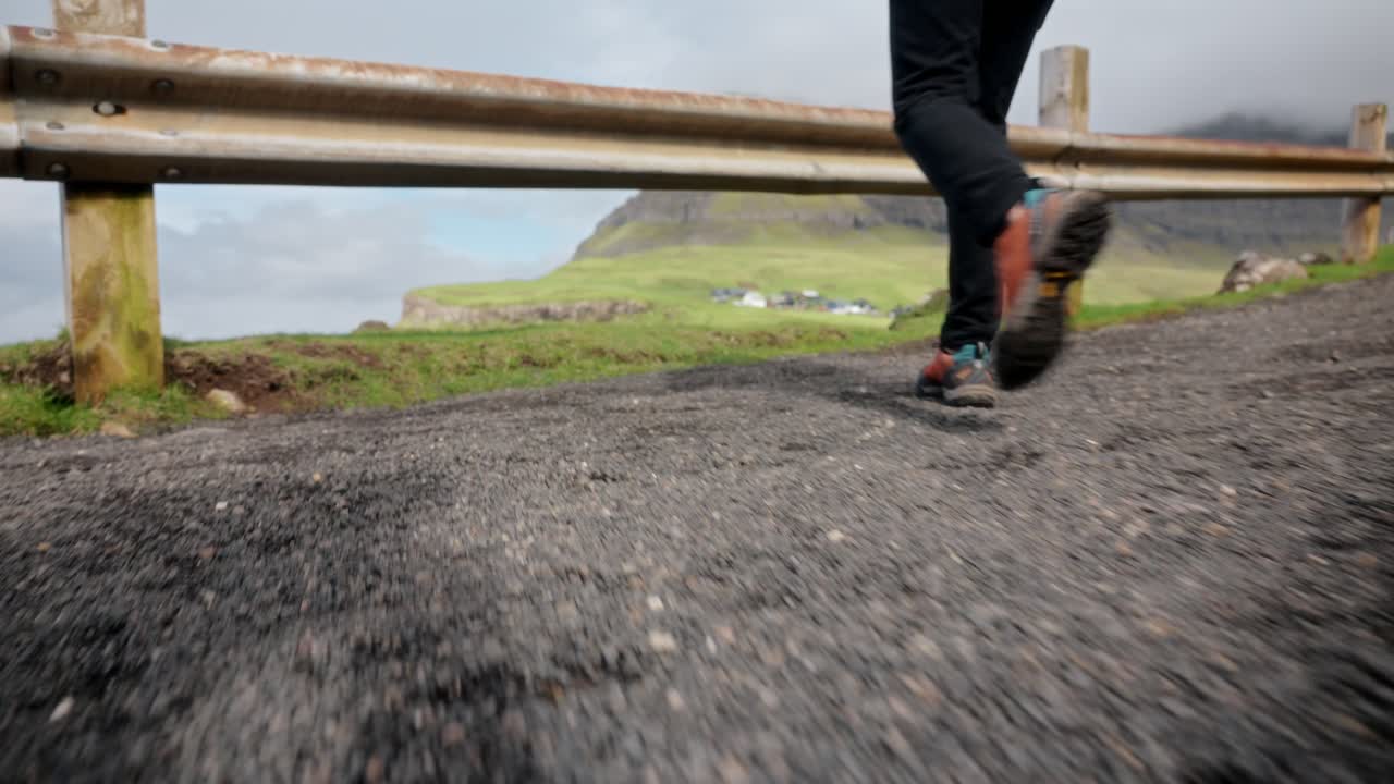 A person walking on a quiet rural road with green cliffs and fields in the background