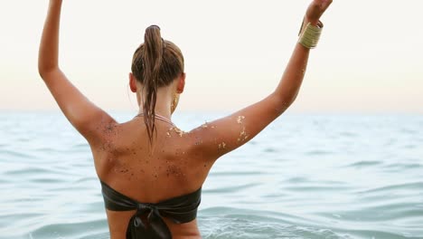 back view of a sexy woman with ponytail standing in the water she turns around and looks in the camera. slow motion shot