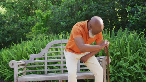 african american senior man with walking stick sitting on a bench in the garden