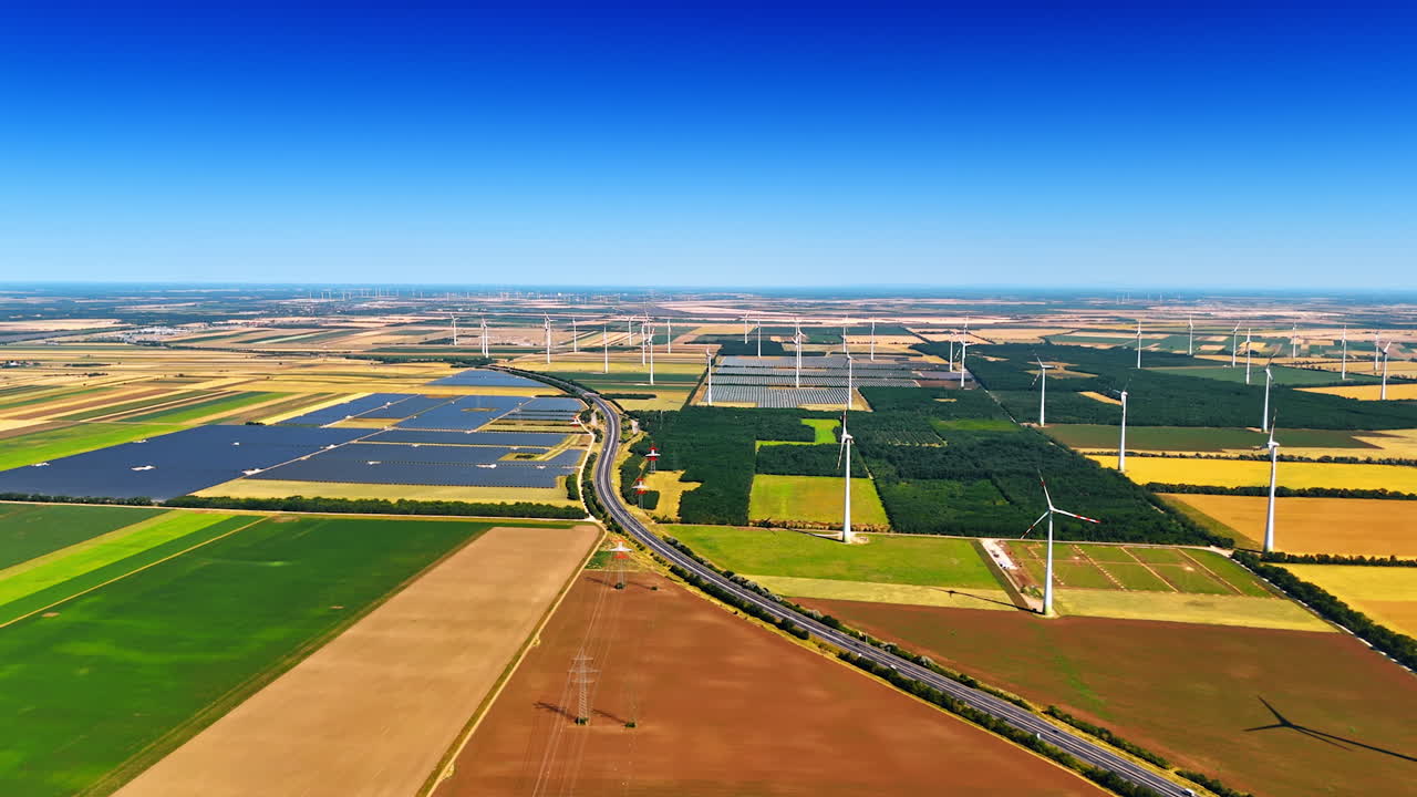Patched fields are crossed by the highway. Aerial perspective on the wind farms and solar panels producing sustainable energy