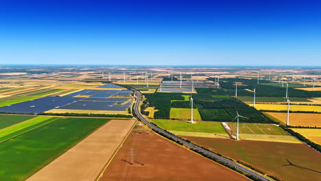 patched fields are crossed by the highway. aerial perspective on the wind farms and solar panels producing sustainable energy